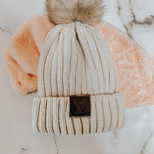 Beige knit beanie with faux fur pom and designer patch